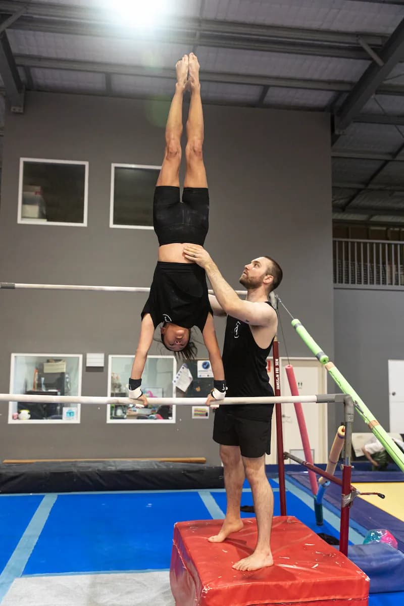 Female gymnast performing a handstand on the uneven bars.