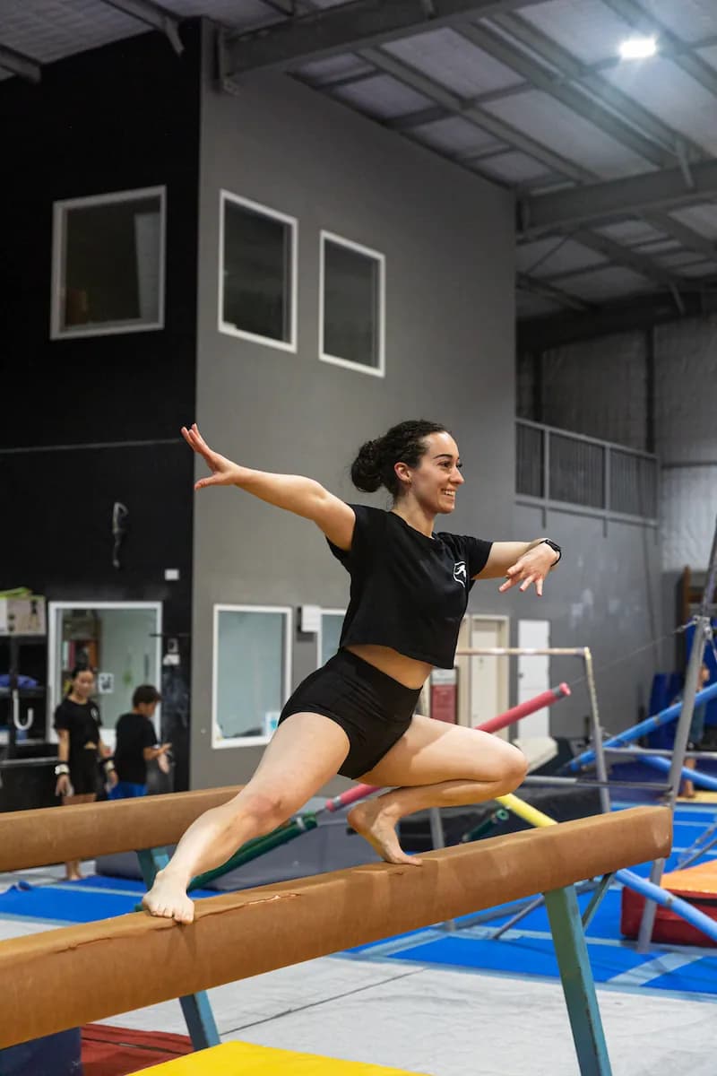 Female gymnast on beam smiling in pose.